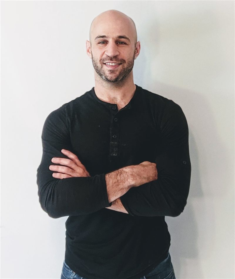 Richard Rabil smiling with arms crossed, standing against a plain wall